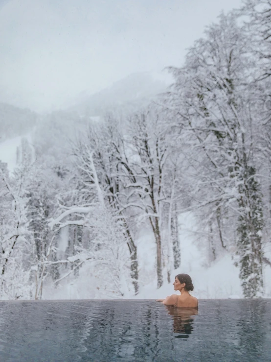 a person in a pool surrounded by snow covered trees, onsens, looking off to the side, sitting down, lush surroundings