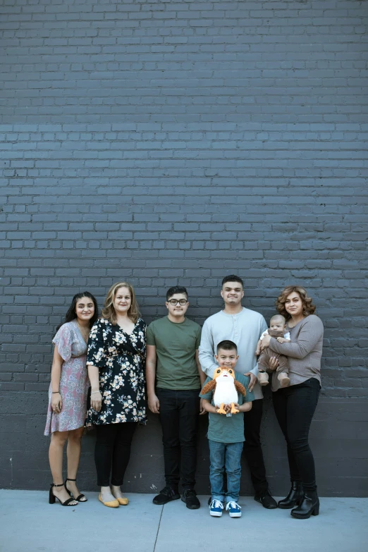 a family poses for a picture in front of a brick wall, by Carey Morris, unsplash, realism, 2 5 6 x 2 5 6 pixels, christian orrillo, grey backdrop, neighborhood