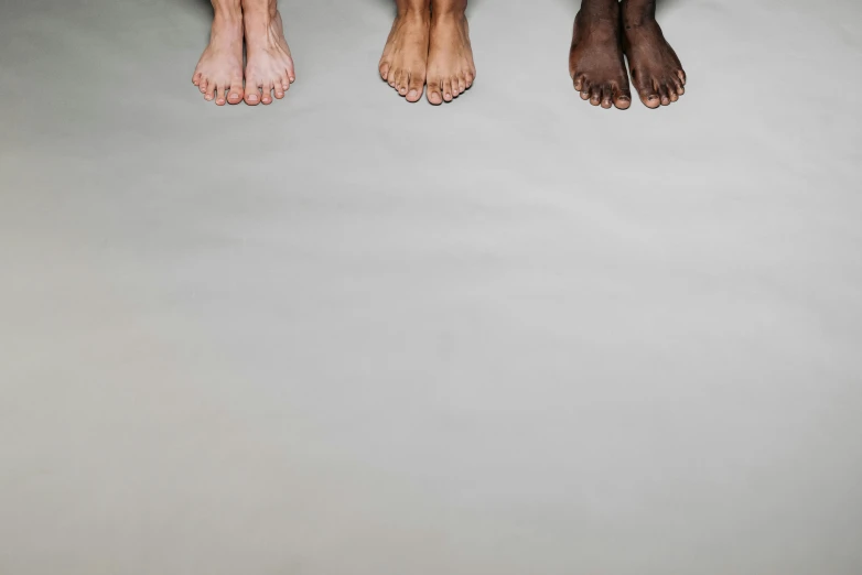 a couple of feet sitting next to each other, trending on pexels, hyperrealism, varying ethnicities, the three moiras, on a gray background, shaven