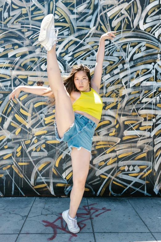 a woman doing a handstand in front of a graffiti wall, wearing yellow croptop, sydney sweeney, body and headshot, slam dancing