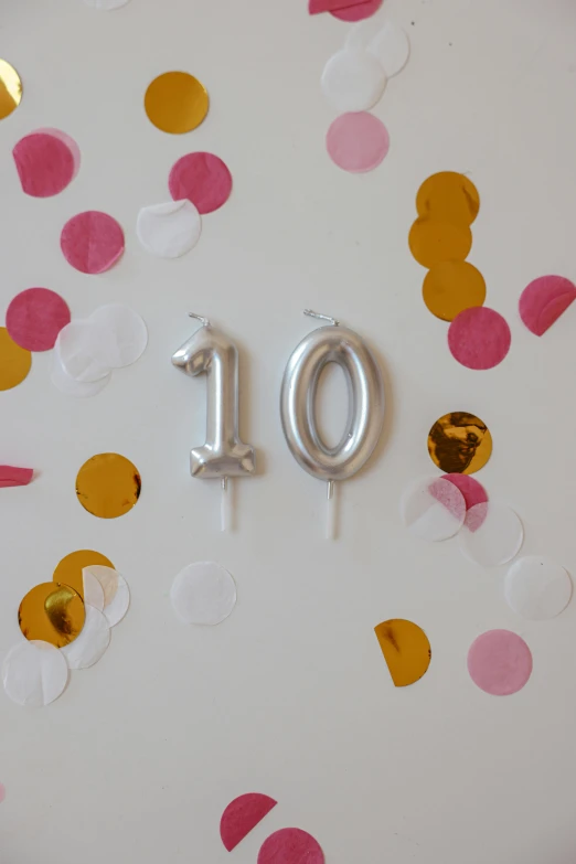 a white plate topped with lots of confetti, golden number, satin silver, 1 0, candle