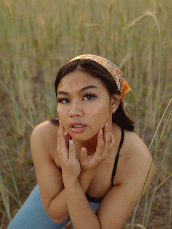 a woman sitting in a field of tall grass, an album cover, inspired by Fernando Amorsolo, unsplash, visual art, 🤤 girl portrait, bandana, hollow cheeks, orange hue