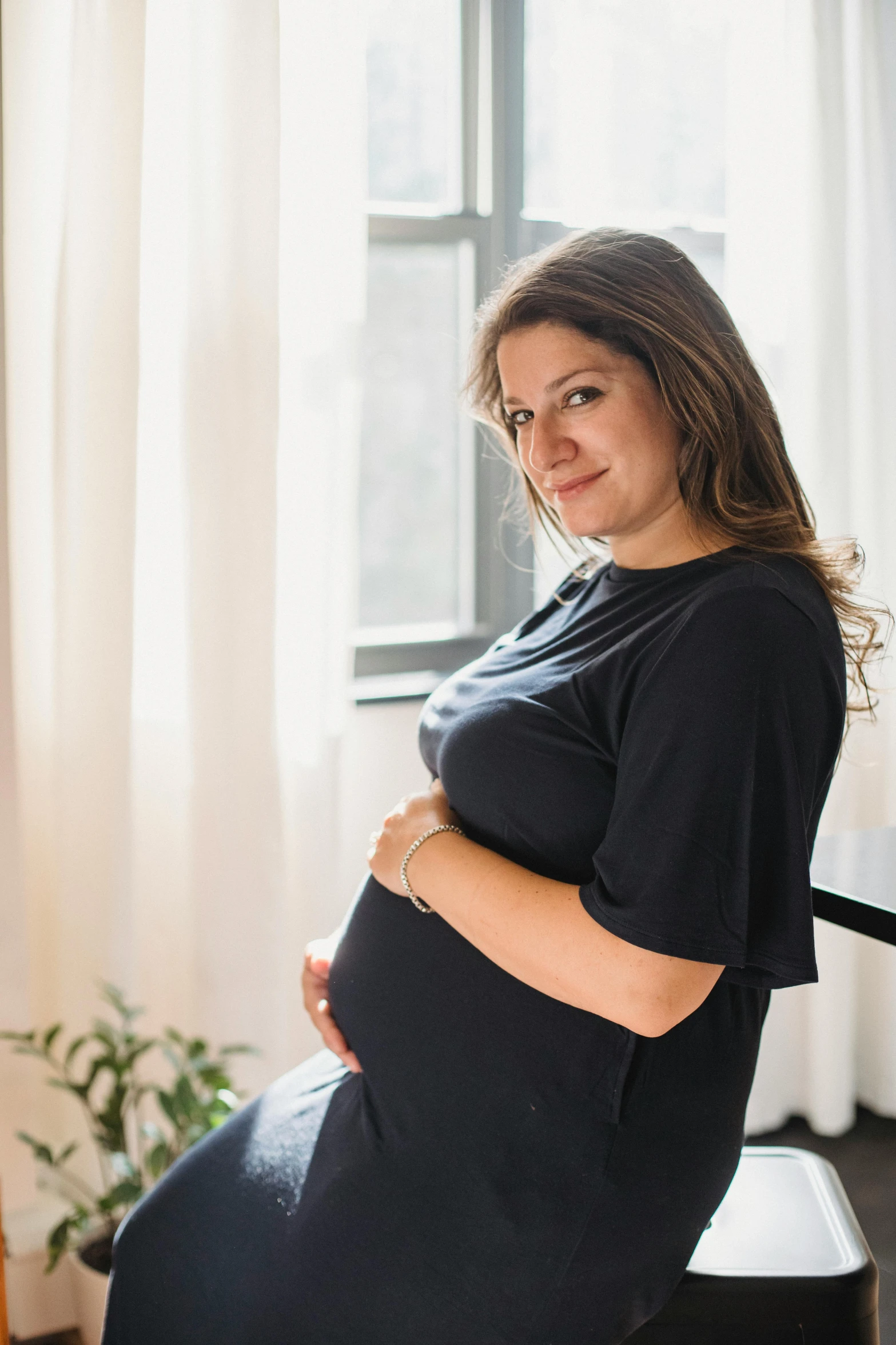 a pregnant woman sitting on a chair in front of a window, by Nina Hamnett, happening, wearing black tshirt, satisfied pose, promo image, multiple stories