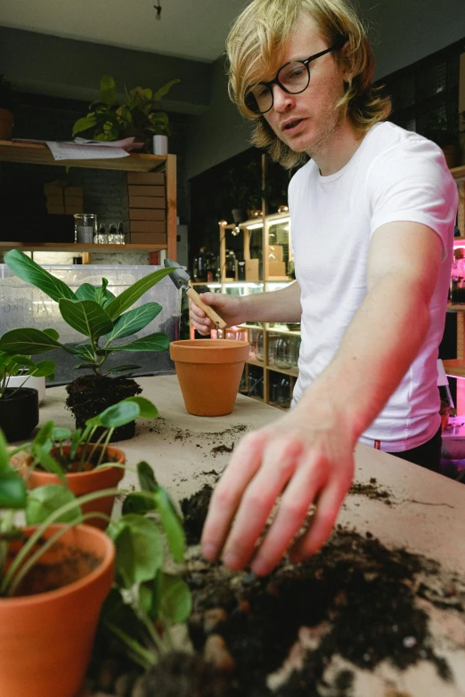 a woman standing over a table filled with potted plants, unsplash, process art, low lighting, lachlan bailey, hands on counter, person in foreground