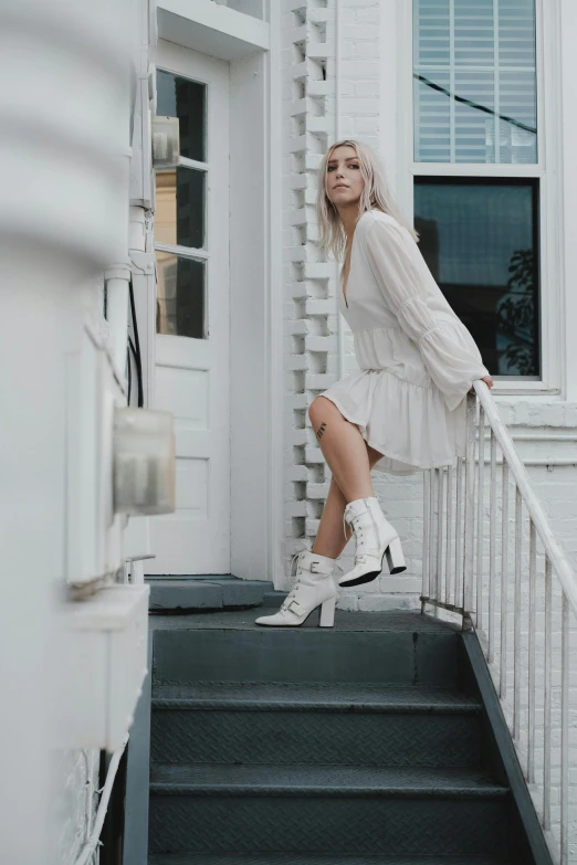 a woman standing on the steps of a house, an album cover, by Sara Saftleven, pexels contest winner, wearing heels and white dress, wearing boots, flowing white hair, female streetwear blogger