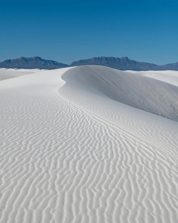 a white sand dune in the desert with mountains in the background, white stripes all over its body, white foam, curving, limestone