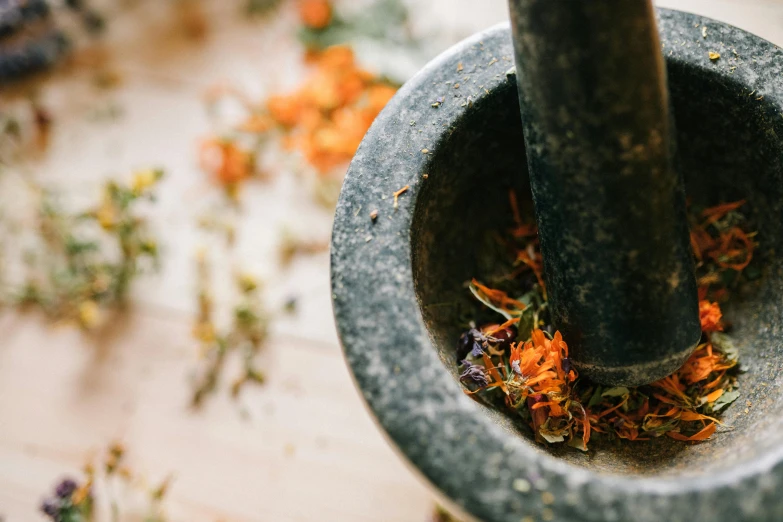 a mortar filled with flowers sitting on top of a table, trending on pexels, dried herbs, gray and orange colours, pestle, swirling around