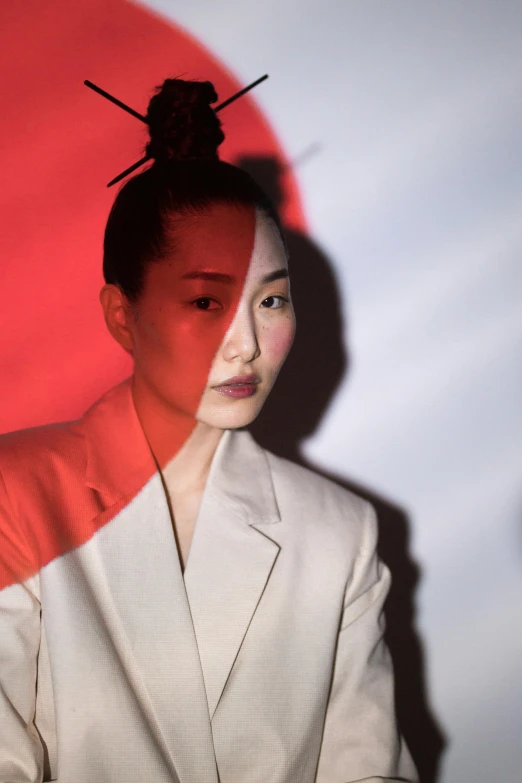 a woman standing in front of a red and white background, an album cover, inspired by Gao Cen, trending on pexels, ethnicity : japanese, reflecting light, girl in suit, nationalist