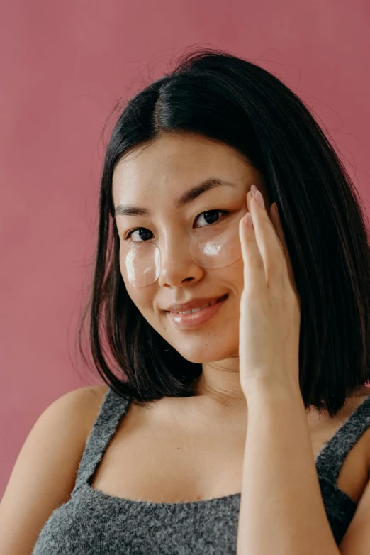 a woman holding her hand up to her face, trending on pexels, renaissance, asian face, cream dripping on face, plain background, hand on cheek
