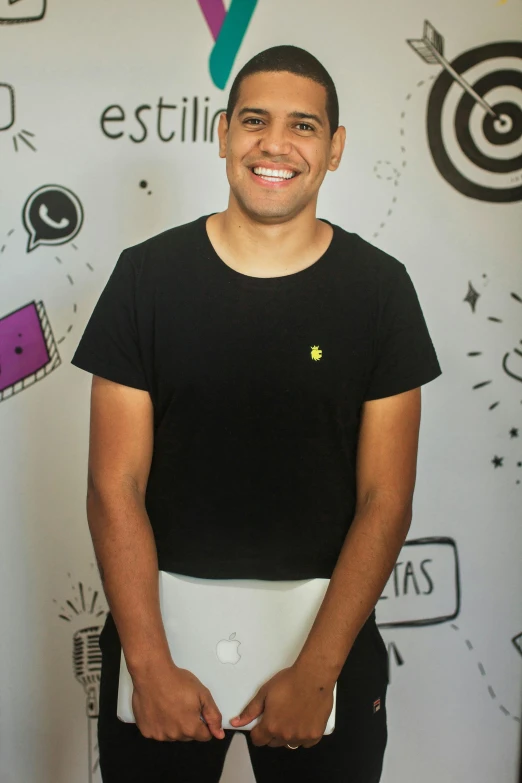 a man standing in front of a wall with a laptop, by Alejandro Obregón, reddit, wearing a black shirt, impish smile, white skirt and barechest, cmyk