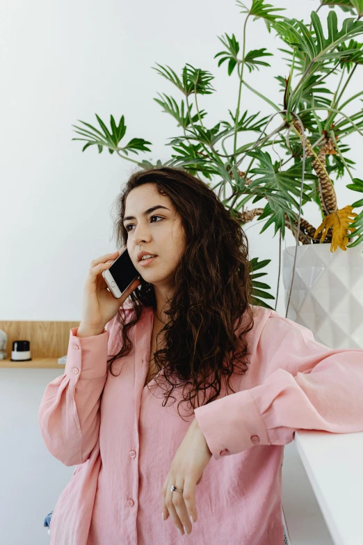 a woman talking on a cell phone next to a potted plant, trending on pexels, renaissance, pink shirt, young middle eastern woman, wavy hair spread out, sitting on a lab table