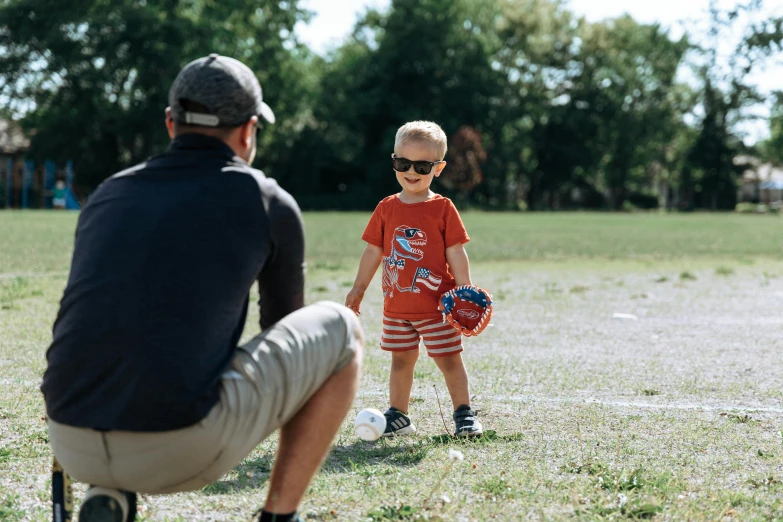 a little boy standing next to a man on a field, wearing shorts and t shirt, clutch yo - yo, shades, father figure image