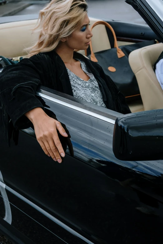 a woman sitting in the driver's seat of a convertible car, trending on unsplash, happening, jet black tuffe coat, wearing a luxurious velvet robe, bottom body close up, leaning on door
