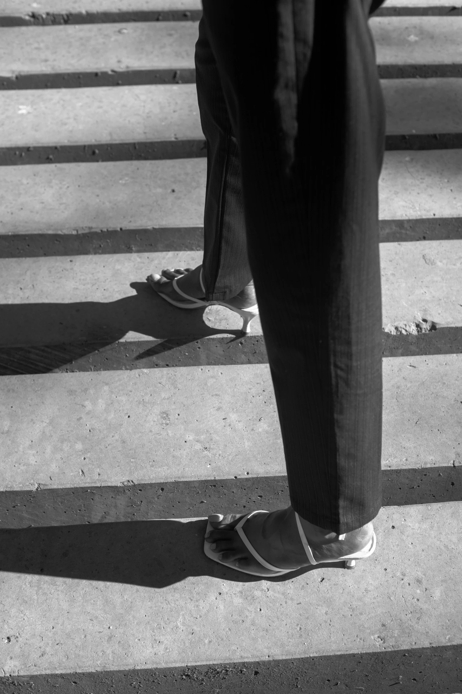 a black and white photo of a person walking across a crosswalk, a black and white photo, inspired by Louis Stettner, photorealism, close-up on legs, 1996), late afternoon sun, coming down the stairs