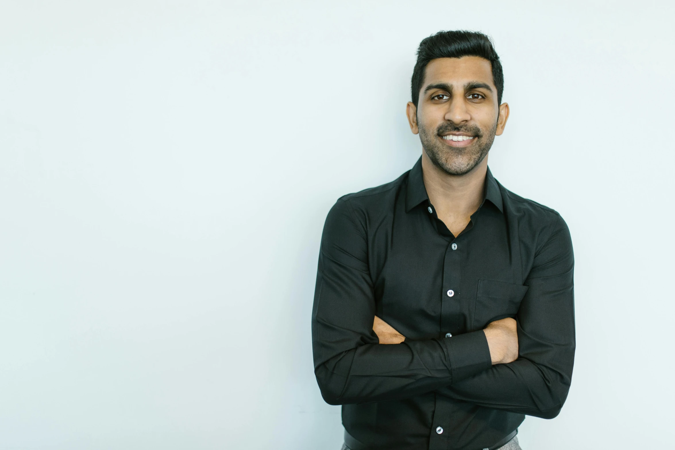 a man in a black shirt standing with his arms crossed, unsplash, hurufiyya, smiling slightly, vishnu, in front of white back drop, ignant