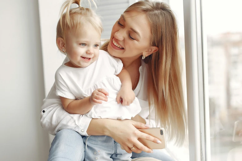 a woman sitting on a window sill holding a baby, pexels contest winner, smiling girl, blond, 15081959 21121991 01012000 4k, instagram post