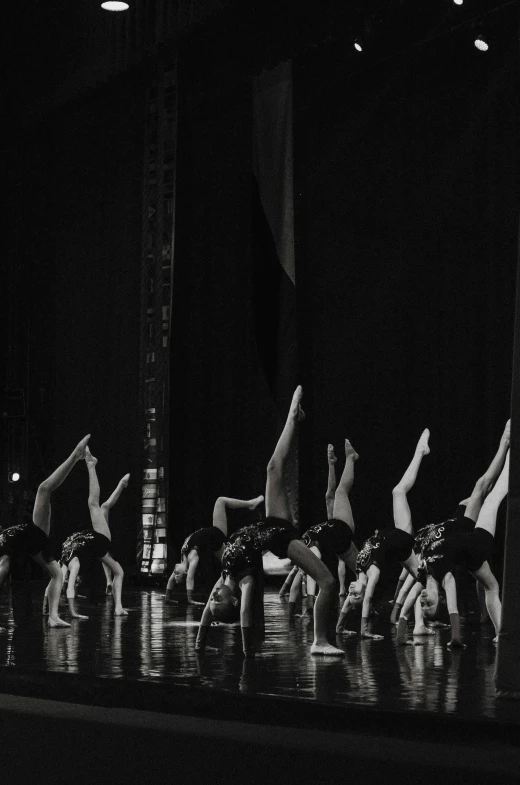 a group of people standing on top of a stage, a black and white photo, unsplash, arabesque, doing splits and stretching, low quality photo, bum, reflection