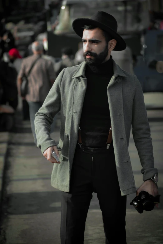 a man standing on a street holding a camera, a colorized photo, inspired by Carlo Mense, rugged beard, grey turtleneck coat, wearing an ammo belt, black stetson and coat