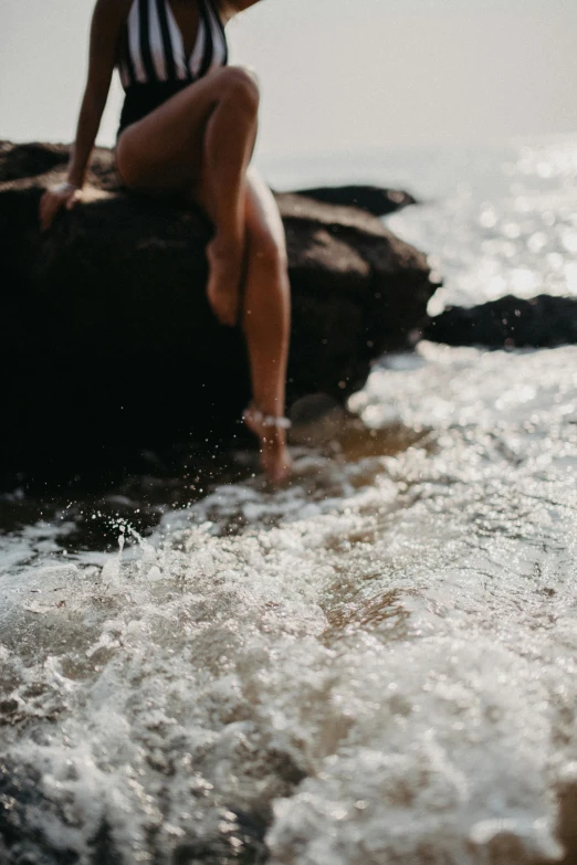 a woman sitting on top of a rock next to the ocean, trending on unsplash, happening, wet shiny skin, foamy waves, close-up on legs, play of light