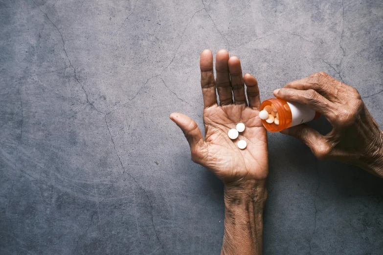 a person holding two pills in their hands, by Matija Jama, trending on pexels, hyperrealism, looking old, raising an arm, agent orange, destitute