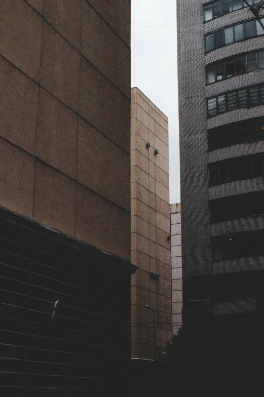 a couple of tall buildings next to each other, a photo, by Pablo Rey, unsplash, brutalism, beige and dark atmosphere, low quality grainy, high quality upload, alleys