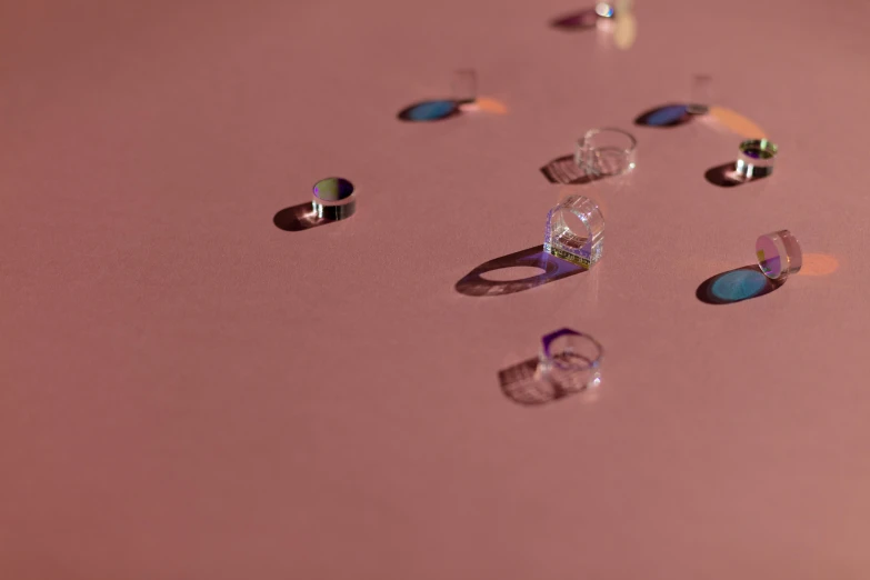 a bunch of rings sitting on top of a table, a hologram, inspired by Lucio Fontana, trending on pexels, holography, minimal pink palette, floating bubbles, detail shot, lying scattered across an empty