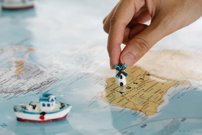 a small toy car sitting on top of a map, boats in the water, back of hand on the table, zoomed in, coastal