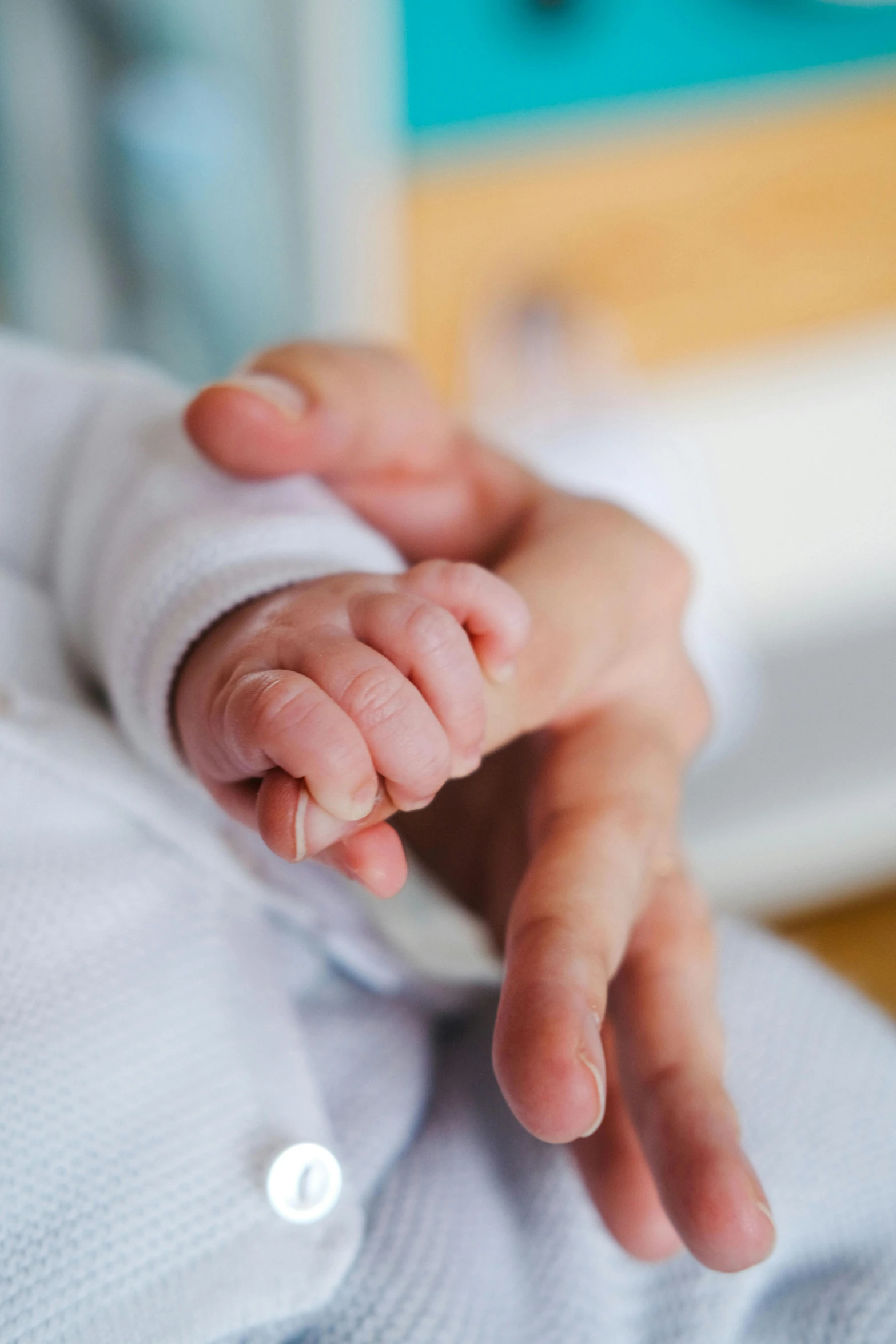 a close up of a person holding a baby's hand, wearing a white hospital gown, solemn gesture, small, next gen