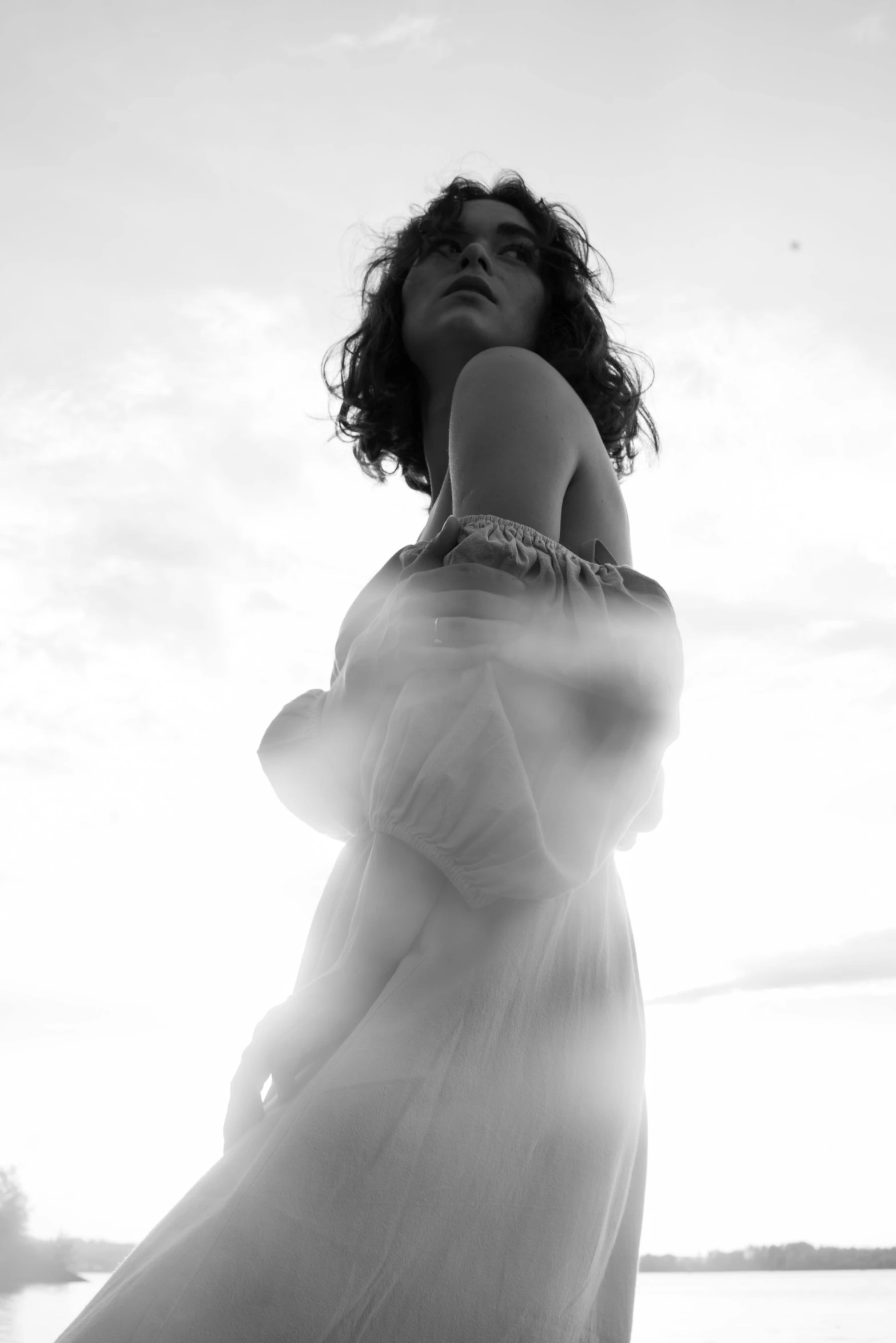 a woman standing on top of a beach next to the ocean, a black and white photo, inspired by Max Dupain, with haunted eyes and curly hair, ethereal angelic being of light, alternate album cover, nathalie emmanuel