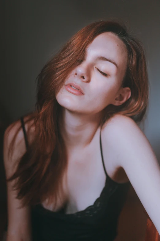 a woman sitting on a bed with her eyes closed, a picture, inspired by Elsa Bleda, trending on pexels, renaissance, ( redhead, she is wearing a black tank top, 🤤 girl portrait, pale thin lips