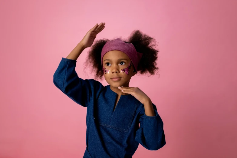 a little girl standing in front of a pink wall, trending on pexels, turban, afro futuristic, greeting hand on head, indigo