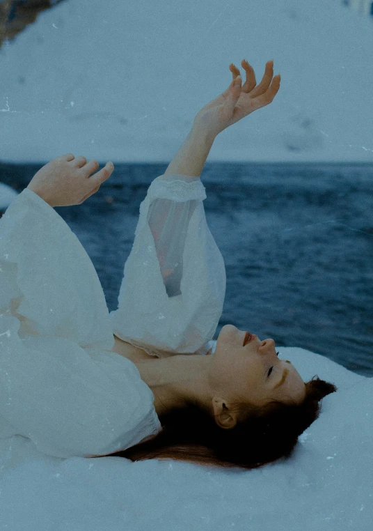 a woman laying on top of a snow covered ground, an album cover, inspired by Elsa Bleda, unsplash, renaissance, floating in the ocean, sansa, crying and reaching with her arm, movie still frame