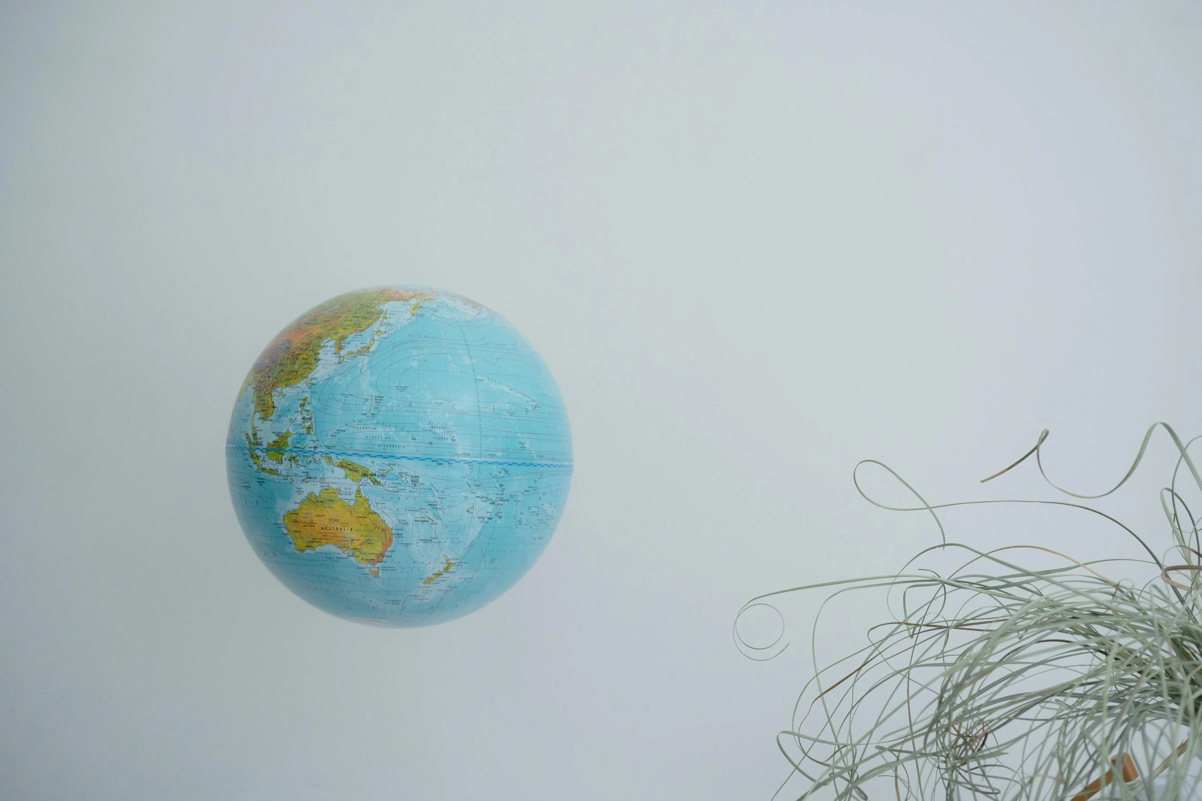 a globe sitting on top of a table next to a plant, by Jessie Algie, trending on unsplash, conceptual art, wires flying in the air, on grey background, floating. greenish blue, taken from a plane