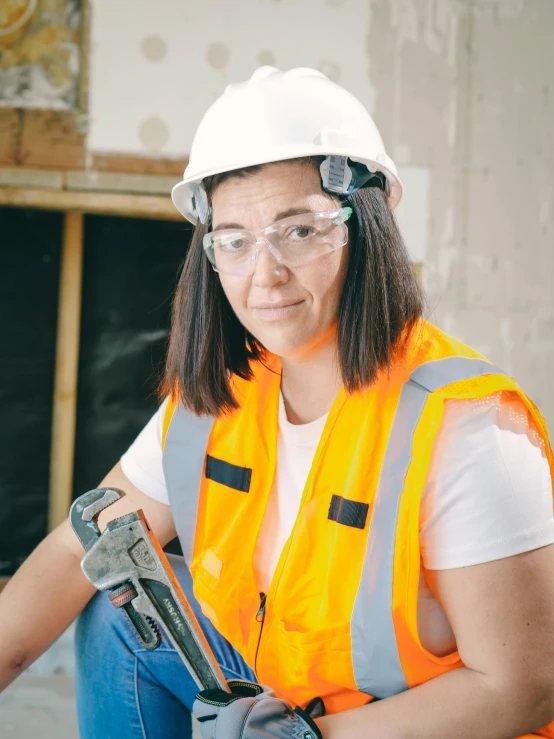 a woman in an orange vest holding a pipe cutter, wearing square glasses, non binary model, profile image, hard hat