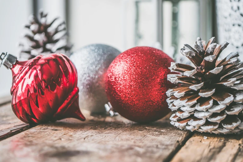 three christmas ornaments sitting on top of a wooden table, pexels contest winner, pinecone, silver red, profile image, various items