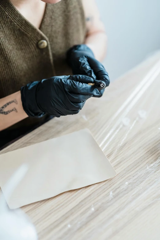 a woman sitting at a table with a tattoo on her arm, plasticien, gloves and jewelry. motion, box cutter, brown paper, packaging