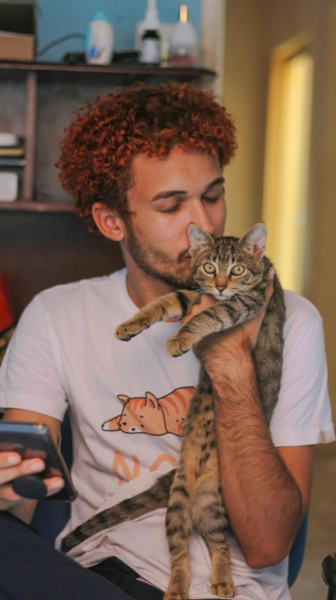 a man sitting on a couch holding a cat, pexels, brown curly hair, wearing a t-shirt, mohamed chahin, gif