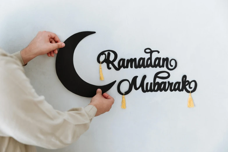 a person holding a paper cutout of a crescent, an album cover, inspired by Sheikh Hamdullah, trending on unsplash, hurufiyya, decorations, “modern calligraphy art, holiday, black