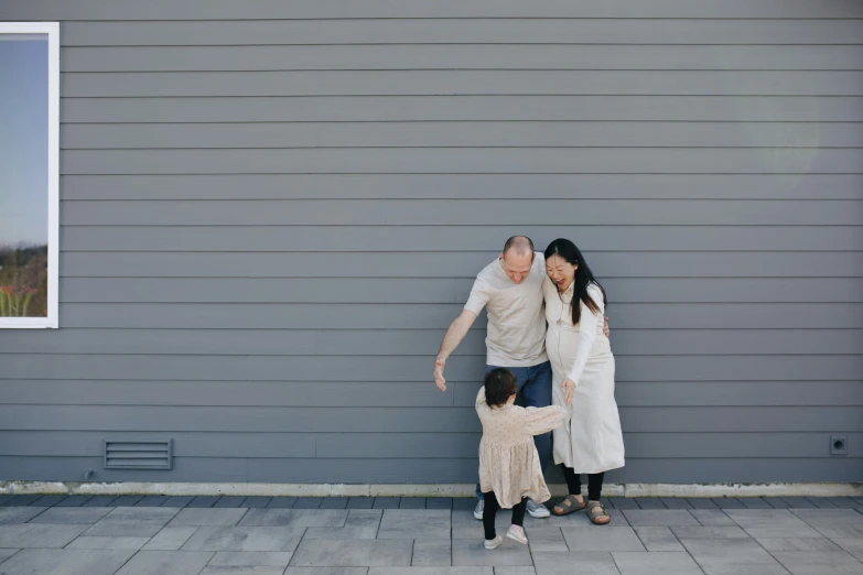 a man and woman standing next to a little girl, pexels contest winner, minimalism, looking around a corner, gray, pregnant, giggling