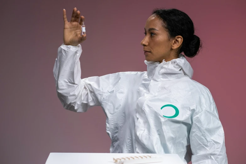 a woman standing in front of a box of doughnuts, by Olivia Peguero, unsplash, holding a syringe, white and teal garment, modular graphene, pictured from the shoulders up