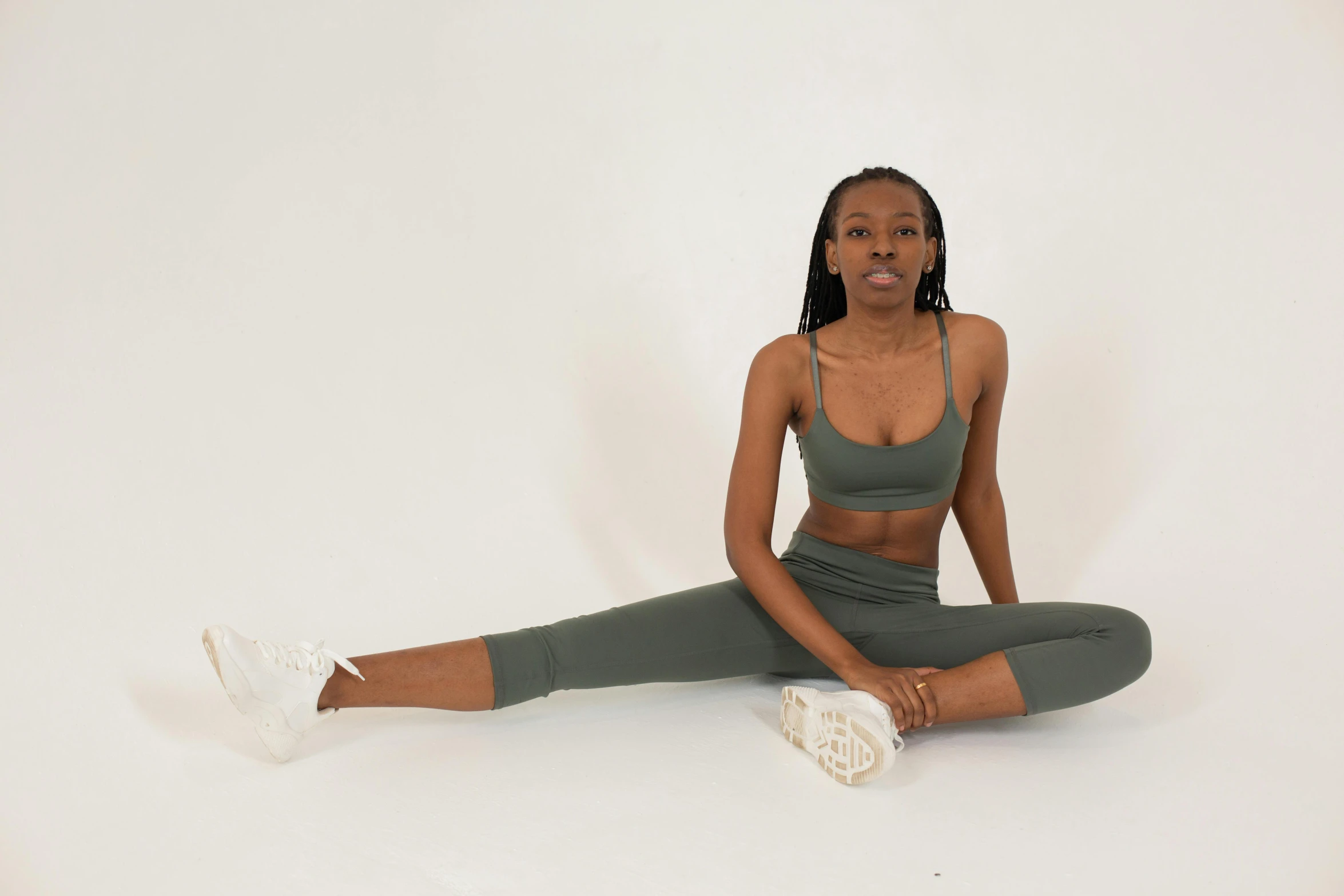 a woman in a sports bra top and leggings sitting on the floor, trending on pexels, renaissance, muted green, adut akech, outlive streetwear collection, full body image