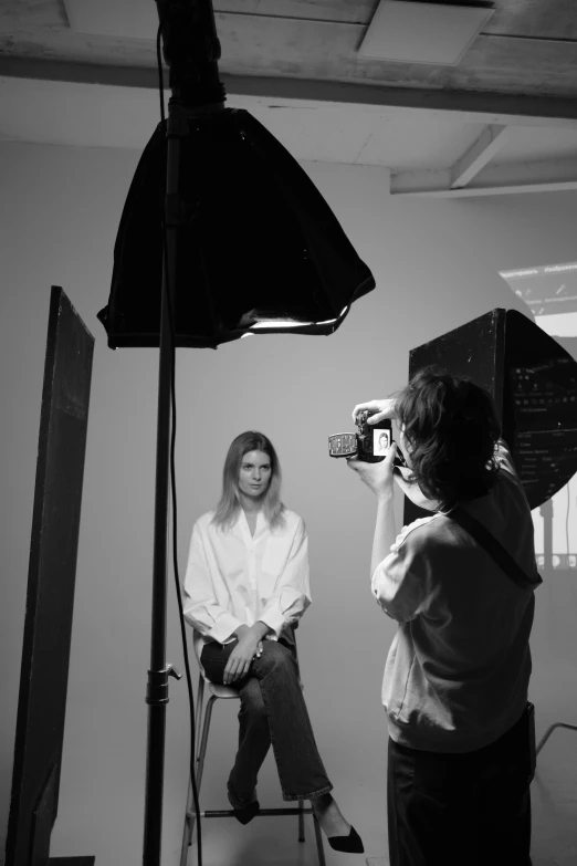 a black and white photo of a woman sitting in front of a camera, a black and white photo, by Clifford Ross, fashion week backstage, softbox key light, sofia coppola, studio medium format photograph