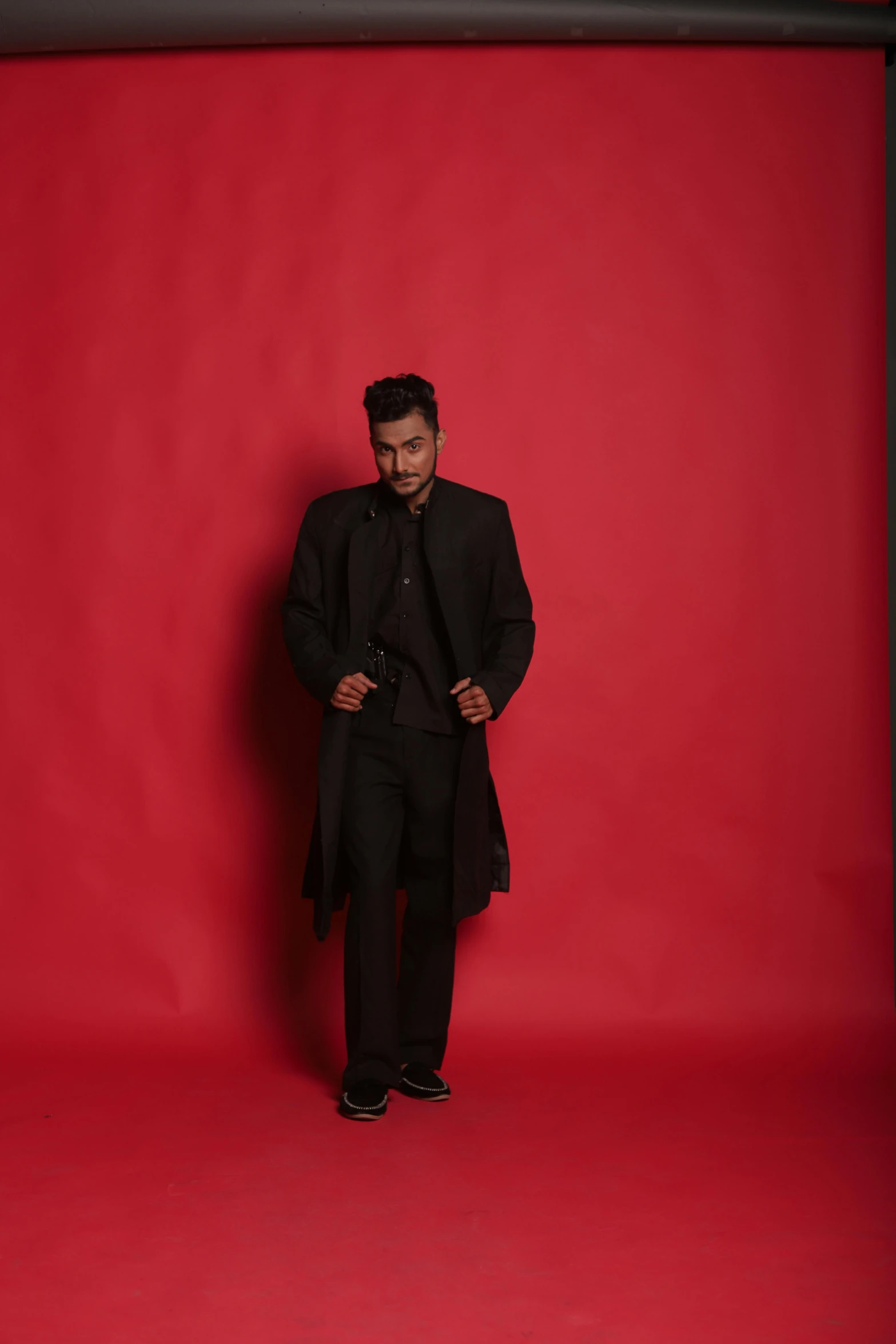 a man standing in front of a red backdrop, an album cover, inspired by Yousuf Karsh, romanticism, he is wearing a black trenchcoat, ranjit ghosh, 15081959 21121991 01012000 4k, model shoot