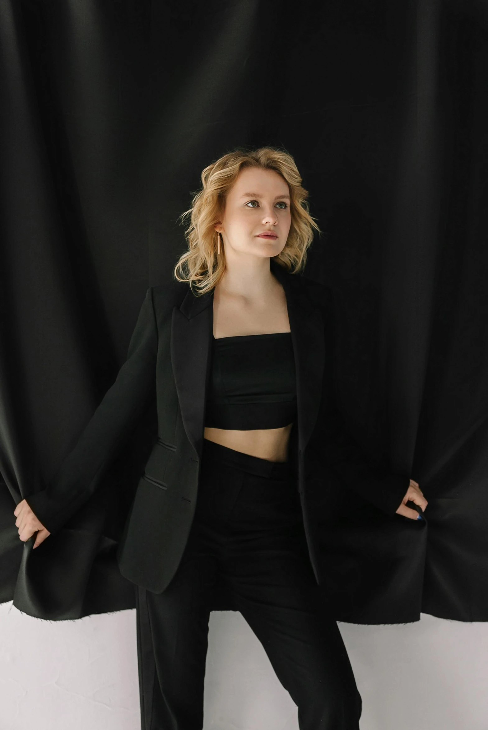 a woman standing in front of a black curtain, black jacket, olya bossak, on a gray background, thicc