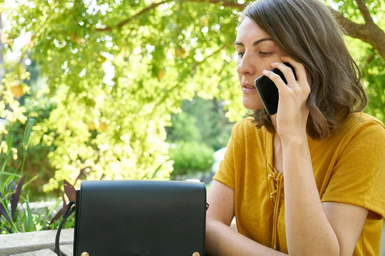 a woman sitting at a table talking on a cell phone, inspired by Clarice Beckett, trending on pexels, figuration libre, holding a gold bag, sydney park, technology and nature, close up shot from the side