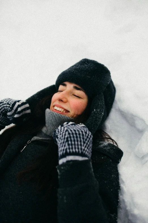 a woman laying in the snow talking on a cell phone, pexels contest winner, smiling down from above, with black beanie on head, raily season, winking