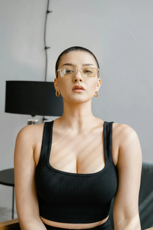 a woman in a black top and glasses sitting on a couch, inspired by Ion Andreescu, trending on pexels, renaissance, asian nymph bald goddess, perfect body and face, square face, maxim sukharev