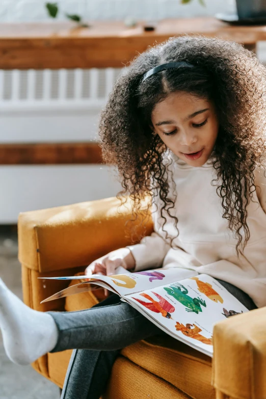 a little girl sitting in a chair reading a book, pexels contest winner, art & language, yellow and orange color scheme, on a couch, schools, casually dressed