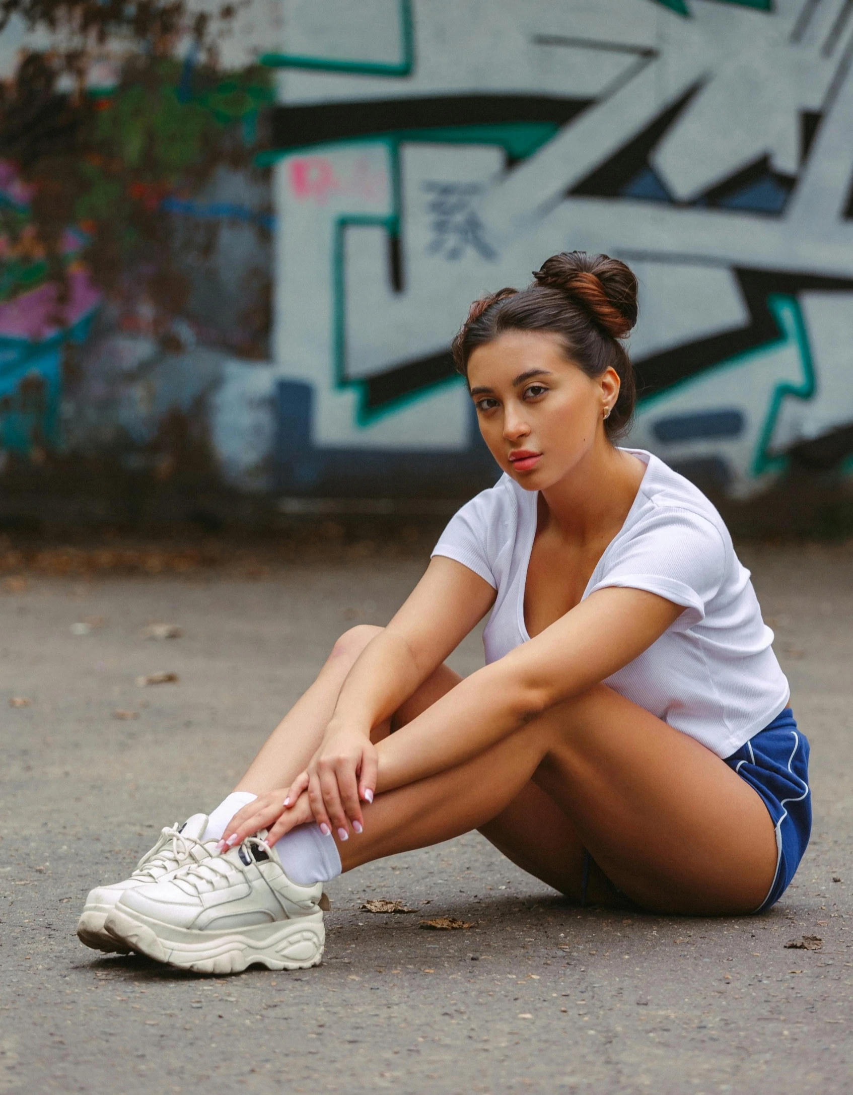 a woman sitting on the ground in front of a graffiti wall, tan skin a tee shirt and shorts, wearing white sneakers, 5 0 0 px models, charli xcx