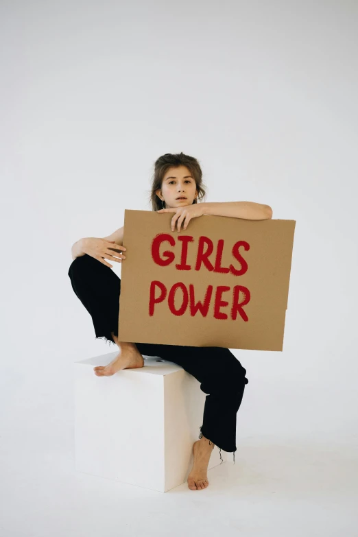 a woman holding a sign that says girls power, an album cover, trending on pexels, hailee steinfeld, alessio albi, electricity superpowers, immature